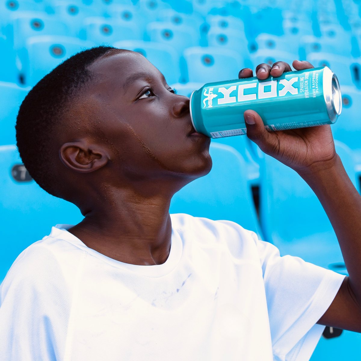 The young player drinks from a turquoise KNOX can in front of the stadium seats